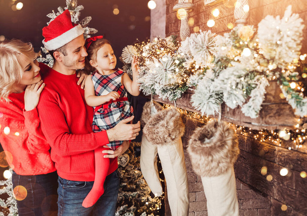 Famiglia di Natale con bambino sorridente vicino all'albero di Natale. Soggiorno decorato da albero di Natale e regalo scatole, la luce dare atmosfera accogliente. Vacanze di Capodanno
 - Foto, immagini