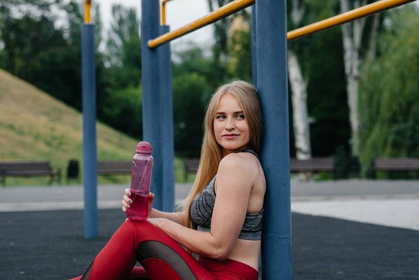 Σέξι κοπέλα κάνει σπορ και πίνει νερό στην ύπαιθρο. Γυμναστική. Υγιής τρόπος ζωής - Φωτογραφία, εικόνα