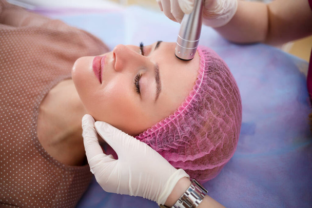 Facial skin care. Young beautiful woman with gets procedure in a beauty salon. Ultrasonic anti-aging cavitation, rejuvenation, lifting procedure. Beauty concept - Photo, Image