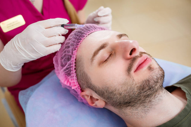 Egy kozmetikus nő ultrahangos arctisztítást végez egy fiatal férfinak a klinikán. Szoros kép és kézügyességi portré, közelkép. Eljárás a szépségszalonban. - Fotó, kép