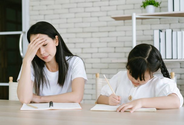 Upset Asian mother is angry to little daughter teach and doing homework writing and reading. Her don't understand while sitting on desk at home. Children education problem, parent and child conflict. - Valokuva, kuva