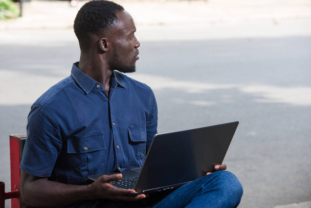 Молодой человек сидит на улице с ноутбуком и смотрит что-то удивленное. - Фото, изображение