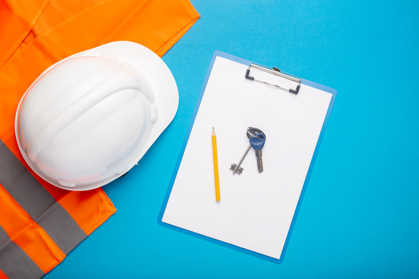 Construction hat, signal vest, apartment keys and clipboard on a light blue background. Concept for construction, renovation work, new building, purchase of an apartment. Banner. Flat lay, top view. - Photo, Image