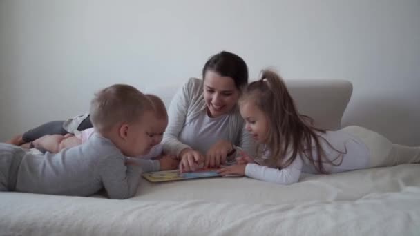 Dzieciństwo, macierzyństwo, koncepcja rodzeństwa - Beztroska młoda mama czytać książki bajki ogony dla małych dzieci, syn noworodka bawić się na łóżku, szczęśliwy wesoły śmiech rodziny łaskocze, pocałunek, uściski leżące relaks - Materiał filmowy, wideo