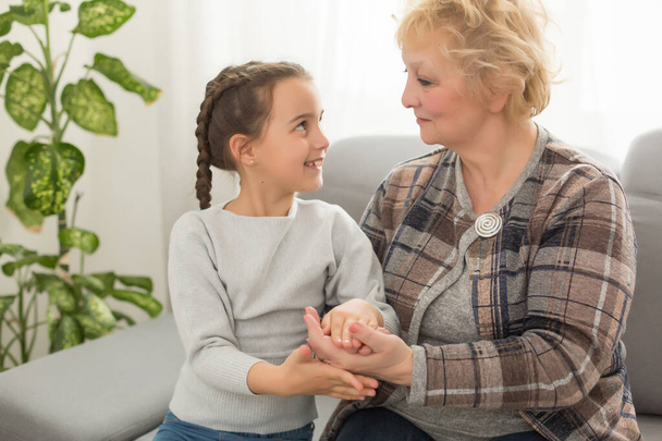 Little granddaughter and happy grandmother giving high five having fun playing together sitting on sofa, smiling grandma granny and preschool grandchild laughing celebrating good relations at home - Фото, зображення