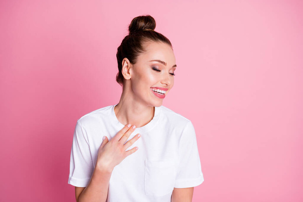 Photo of charming nice crazy lady funny pretty bun summer vacation good mood laughing out loud arm on chest wear casual white t-shirt isolated pastel pink color background - 写真・画像