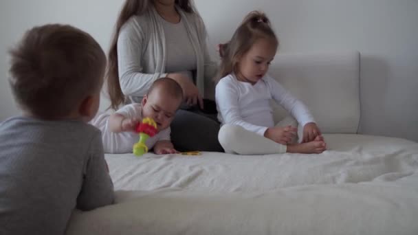 Childhood, motherhood, siblings concept - Carefree young mum combs her little kid daughter hair , son and newborn baby have fun play on bed, happy cheerful family laugh tickles, kiss, hugs lying relax - Footage, Video