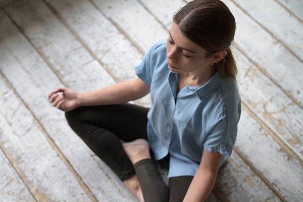 Young woman meditating sitting on the floor in an empty construction apartment, top view - Valokuva, kuva