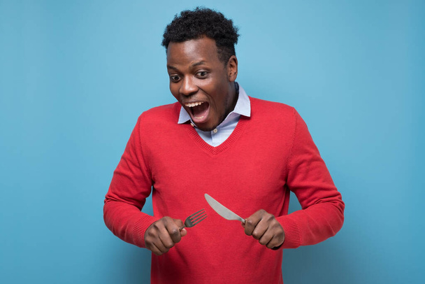 Hongerige Afrikaanse man met bestek vork en mes bij de hand die iets wil proeven - Foto, afbeelding