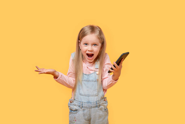 Surprised, happy face, open mouth of a little girl with a phone in her hands. - Foto, afbeelding