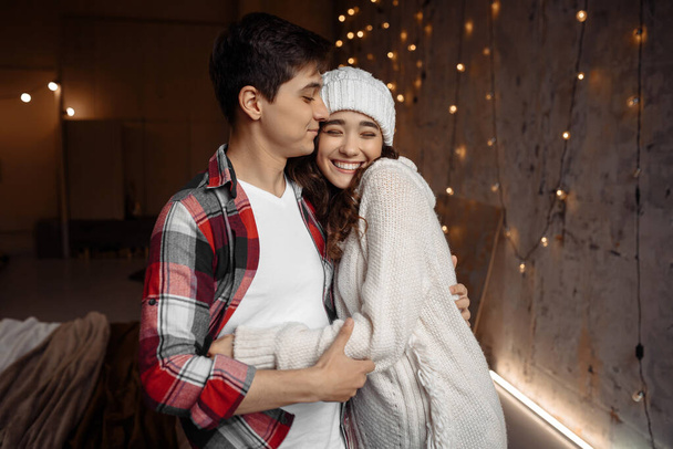 Κομψό ευτυχισμένο ζευγάρι που αγκαλιάζονται και περνάνε την παραμονή των Χριστουγέννων μαζί. Χαρούμενες στιγμές στις χειμερινές διακοπές. Εποχιακοί χαιρετισμοί. Έννοια διαφήμισης - Φωτογραφία, εικόνα