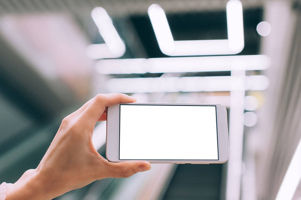 Mock up of a smartphone in hand, on the background of an escalator in a shopping center and luminous lamps - Foto, imagen