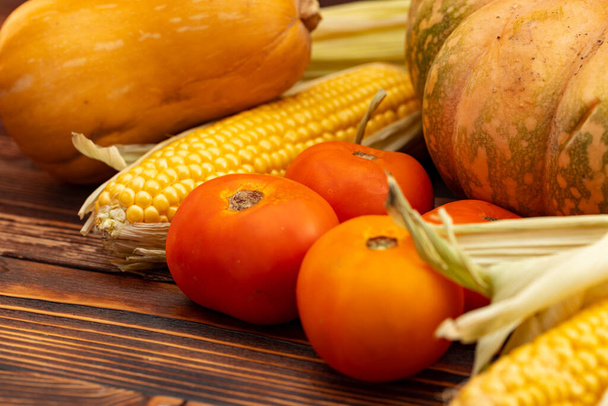 Pumpkin, corn and tomatoes on brown wooden background - Fotografie, Obrázek