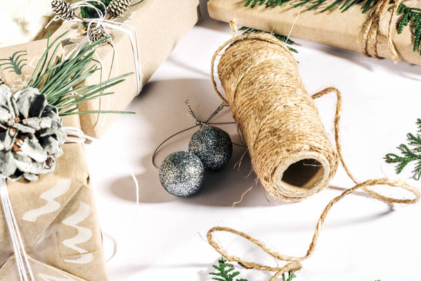 Weihnachtlicher Hintergrund mit handgefertigten Geschenkschachteln, Seilklemmen und Dekorationen mit Tannenzapfen und Zweigen in Weiß. Vorbereitung auf die Ferien... - Foto, Bild