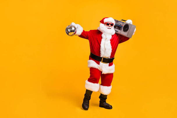 Full length photo of funky santa claus with grey beard hold boom box disco ball x-mas christmas jolly holly eve time party wear headwear red cap isolated yellow color background - Фото, зображення