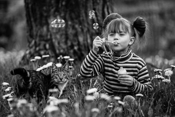 Pikkutyttö leikkii kissan kanssa nurmikolla. Musta ja valkoinen valokuvaus. - Valokuva, kuva