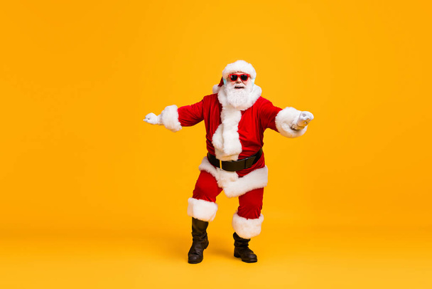 Teljes méretű fotó funky télapó claus szürke szakáll hallgatni x-mas karácsonyi zene dal headset tánc viselet napszemüveg fejfedő sapka elszigetelt felett fényes fény háttér - Fotó, kép