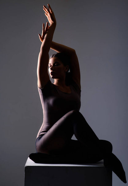 A woman in a yoga pose. Beautiful athletic young female gymnast in sportswear, training, gymnastics element, performs exercises on a dark background. Sports motivation, stretching, physical education - Fotó, kép