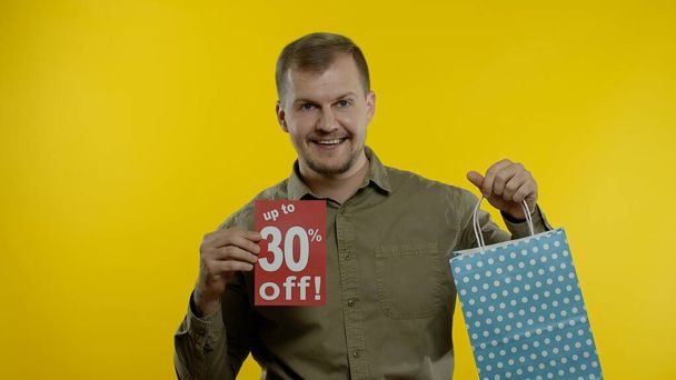 Hombre feliz que aparece hasta 30 por ciento de descuento en la inscripción de la bolsa de la compra, sonriendo, regocijo descuentos - Foto, Imagen