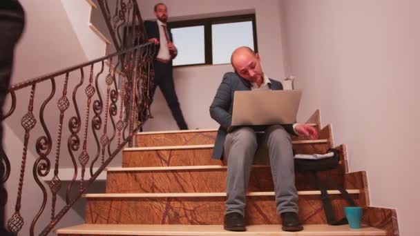 Pisząc na laptopie mówiąc przez telefon siedząc na schodach - Materiał filmowy, wideo
