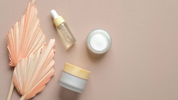 Natural organic cosmetic set. Essential oil dropper bottle, moisturizer cream jars and dry flowers on pastel beige background. Flat lay, top view. - 写真・画像
