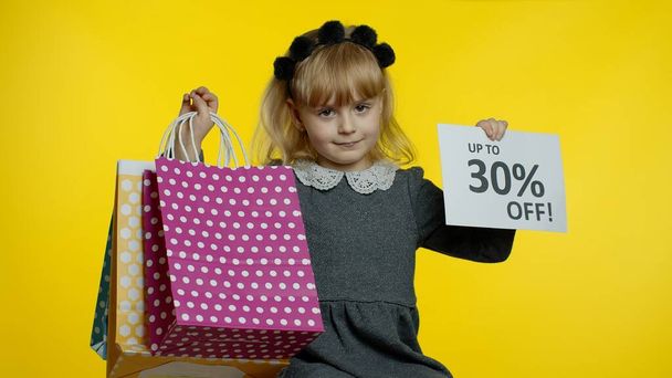 Child girl showing Up To 30 percent Off inscription sign and shopping bags. Teen pupil smiling - Foto, imagen