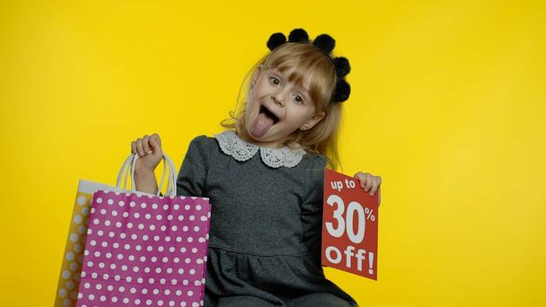 Gyermek lány felbukkan 30 százalékkal olcsóbb felirattal és bevásárlószatyrokkal. Tini tanuló mosolyog - Fotó, kép