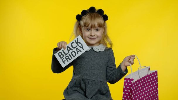 Παιδί κορίτσι με τσάντες ψώνια δείχνει Black Friday επιγραφή, ικανοποιημένος με τις χαμηλές τιμές εκπτώσεις - Φωτογραφία, εικόνα