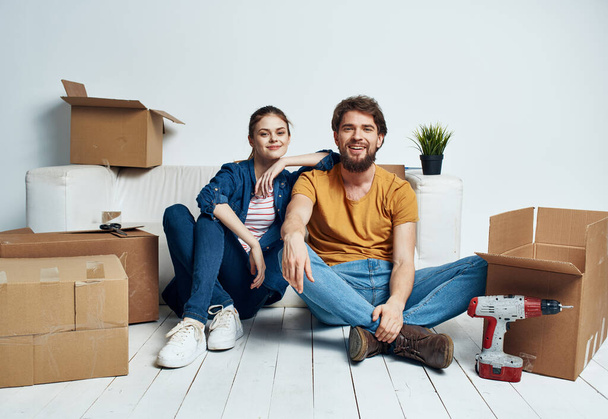 Мужчина и женщина сидят на полу в помещении рядом с диваном и двигают коробки - Фото, изображение