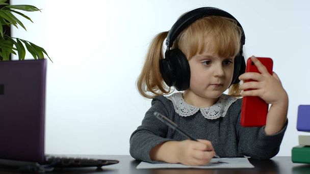 Enfant préscolaire fille distance apprentissage en ligne à la maison. Étudier avec un téléphone portable numérique - Photo, image