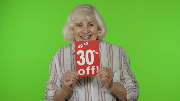 Az idősebb nagymama felbukkan 30% -kal olcsóbban feliratos táblákon, és örül az árengedményeknek. Fekete péntek - Fotó, kép