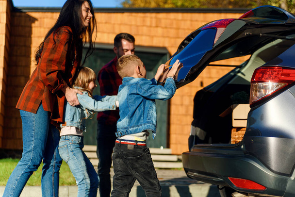 A happy family loads luggage into the trunk of a car when going on a family vacation. - Photo, Image