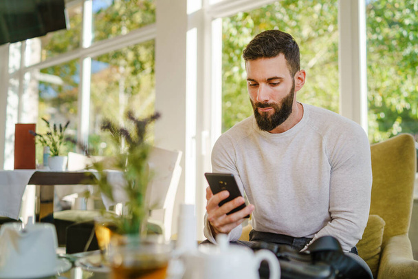 Portrait of adult good looking caucasian man sitting at cafe in day using mobile phone - Male with beard online date on internet while waiting sending love in video call - dating and meeting concept - Foto, immagini
