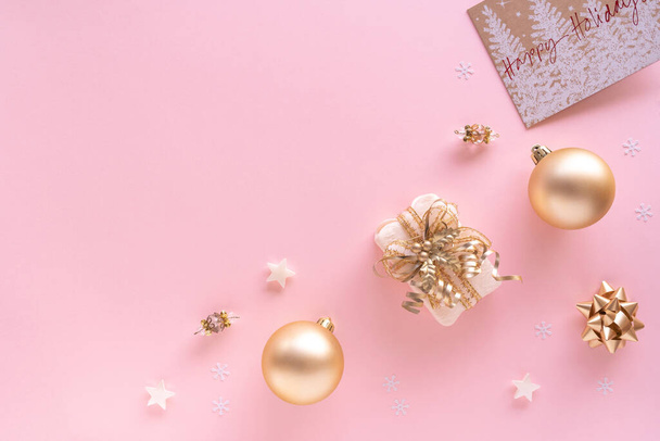 Christmas composition. Gift, baubles, greeting card, golden decorations on pastel pink surface. Christmas, winter, new year concept. Flat lay, top view, copy space, from above. - Foto, Bild