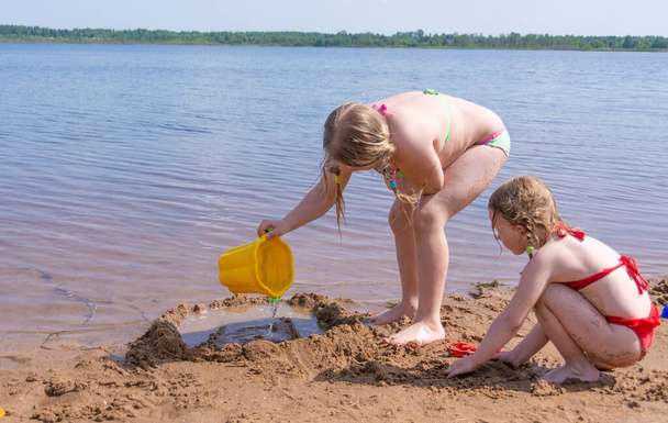 Les filles jouent sur la plage de sable au bord du lac dans la chaleur estivale.  - Photo, image