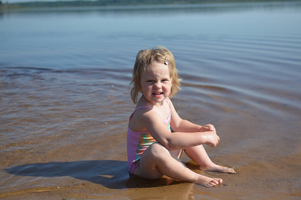Una chica está tomando el sol en una playa de arena en el lago en el calor del verano. - Foto, Imagen