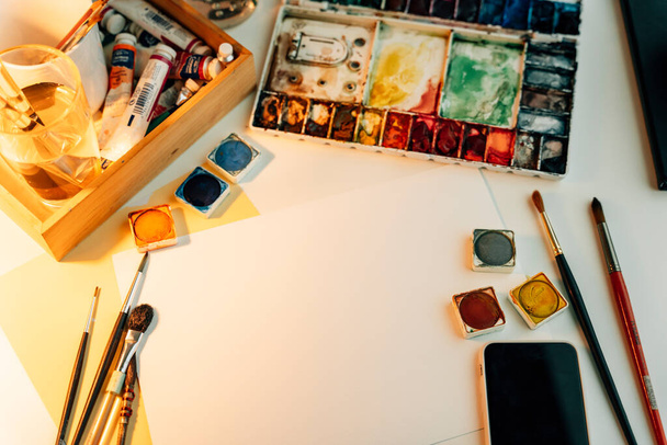 Felülnézet - festőasztal színes festőeszközökkel és papírképpel. - Fotó, kép