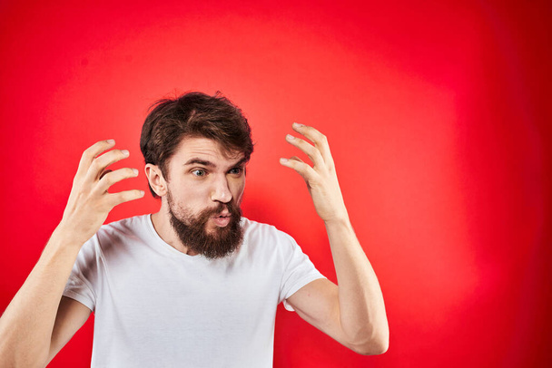 Duygusal sakallı adam elleri beyaz tişörtlü agresiflik, hoşnutsuzluk kırmızı arka planda hareket eder. - Fotoğraf, Görsel