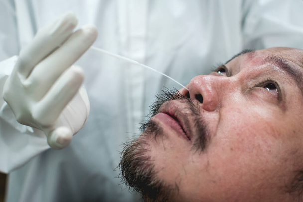 Un hombre asiático tranquilo pero visiblemente preocupado se desnuda de una prueba rápida de hisopo nasofaríngeo covid-19 insertada parcialmente en su nariz. Prueba de hisopo nasal covid auténtica y reacción del paciente. - Foto, imagen
