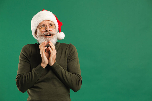 Feliz barbudo moderno Papai Noel mantém as mãos juntas e se alegra com um fundo verde - Foto, Imagem