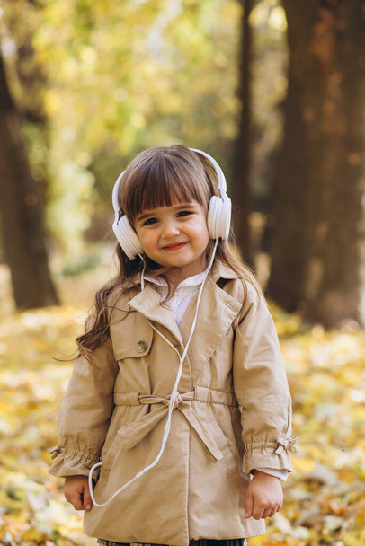 Портрет щасливої дівчинки, що слухає музику на навушниках в осінньому парку
 - Фото, зображення