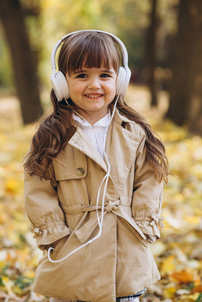 Ritratto di una bambina felice che ascolta musica con le cuffie nel parco autunnale - Foto, immagini