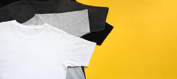 top view stack of black, grey and white (monochrome) t-shirt on yellow background with copy space, flat lay - Fotoğraf, Görsel
