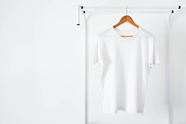 gros plan de t-shirt de couleur blanche accroché sur cintre à vêtements en bois sur porte-vêtements sur fond blanc, espace de copie - Photo, image