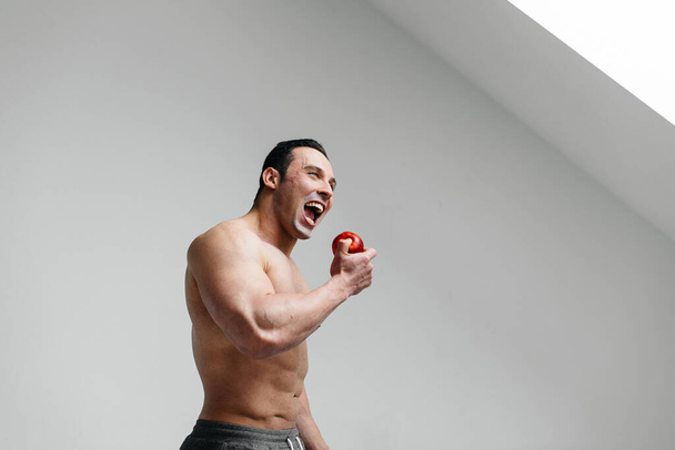 Sporty sexy guy eating fruit on a white background. Diet. Healthy diet - Фото, изображение