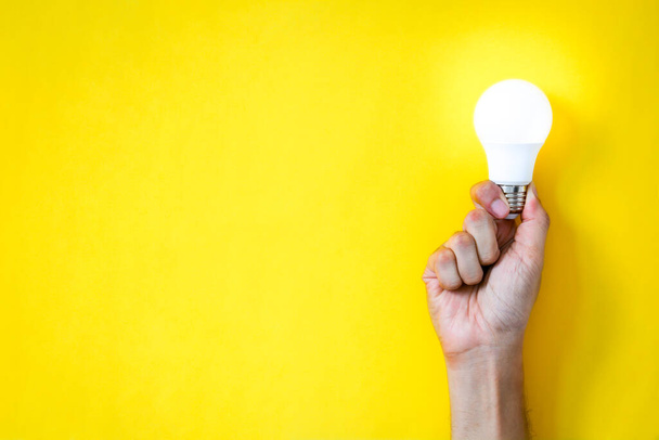 χέρι ανθρώπου κρατώντας λαμπτήρα LED πάνω από κίτρινο χρώμα φόντο με αντίγραφο χώρου, επίπεδη lay, έννοια των ιδεών - Φωτογραφία, εικόνα