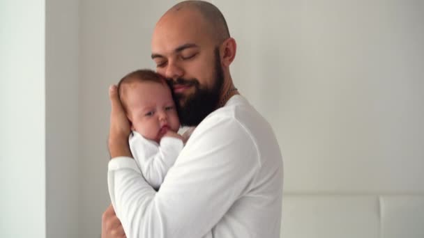 Ένας ευτυχισμένος γενειοφόρος άντρας στέκεται στο δωμάτιο κρατώντας ένα νεογέννητο μωρό στην αγκαλιά του. Έννοια ευτυχισμένων γονέων - Πλάνα, βίντεο