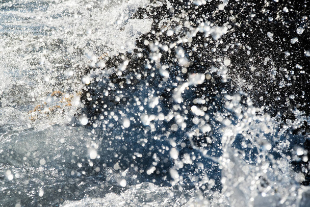 Detalle de una ola rompiéndose en la orilla contra una roca, salpicando muchas gotas de agua. Obturador rápido movimiento congelado. - Foto, Imagen