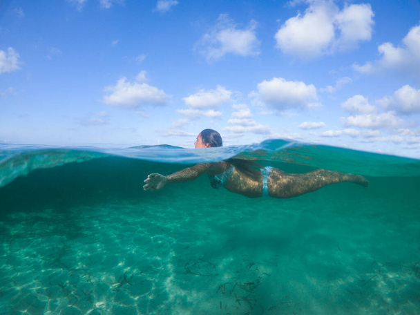 Woman swimming into the sea. View at water level, camera 50% submerged, photo with underwater dome. - Φωτογραφία, εικόνα