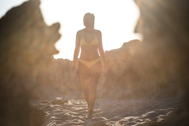 Verlichte vrouw wandelend in een bikini op een strand tussen rotsen met een weemoedige lucht. Een gok. Formentera eiland, Spanje. - Foto, afbeelding